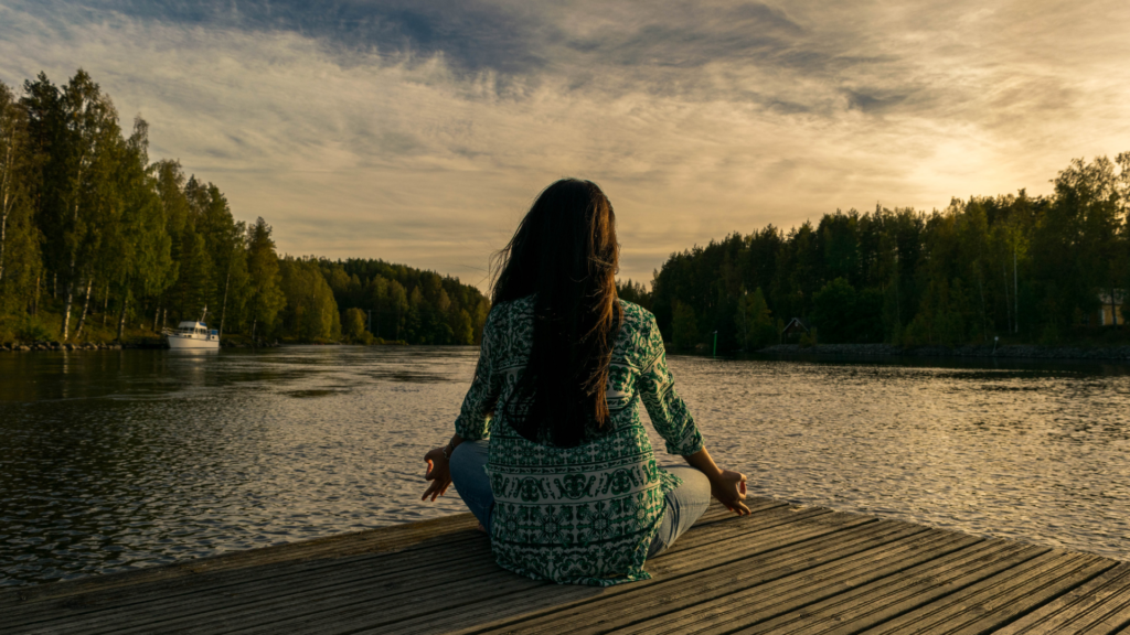 A woman sitting on a dock by a lake meditating