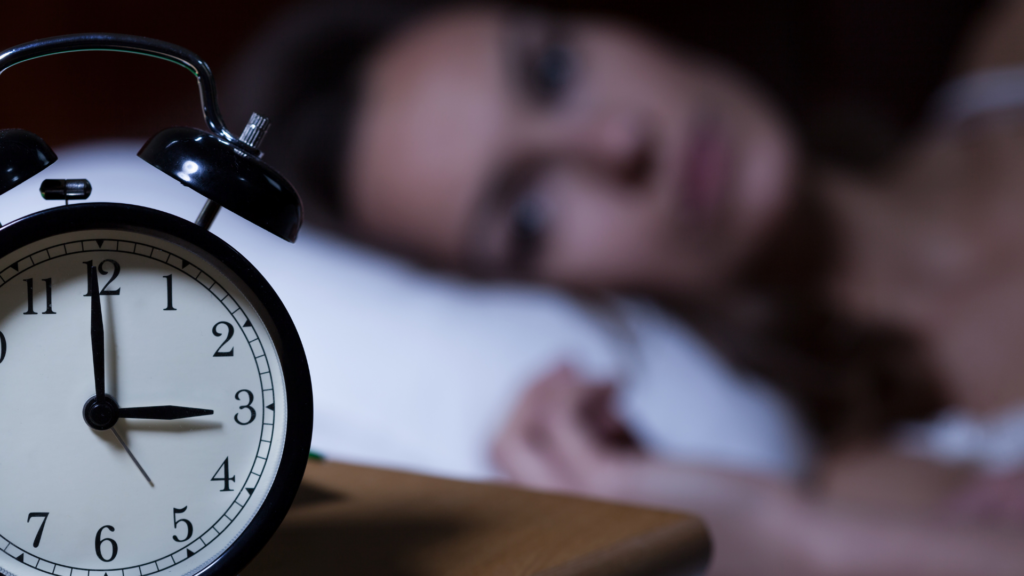 9 Things You Can Do To Improve Your Sleep- Woman laying in her bed awake and an alarm clock in front of her that reads 3 am